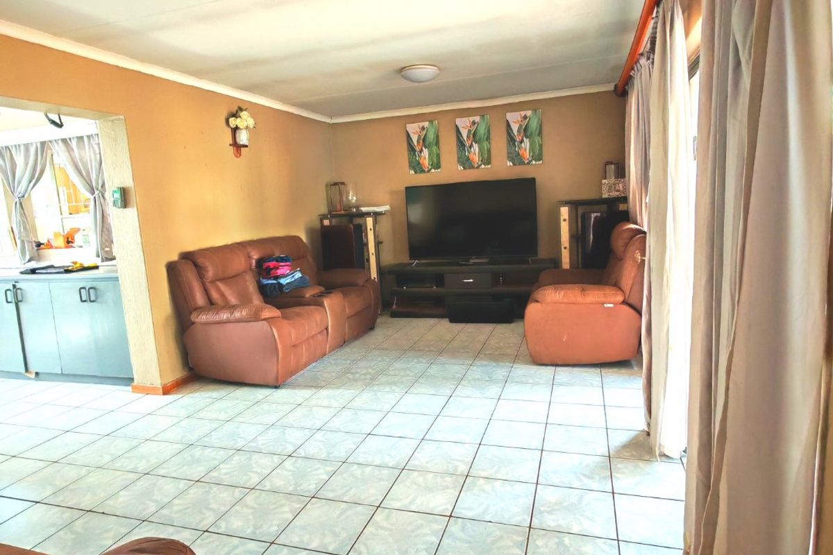 A living room featuring tiled flooring and a sliding glass door, with an open-plan layout connecting to the adjacent kitchen area.