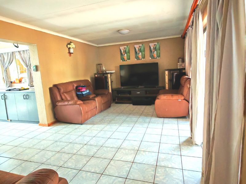 A living room featuring tiled flooring and a sliding glass door, with an open-plan layout connecting to the adjacent kitchen area.