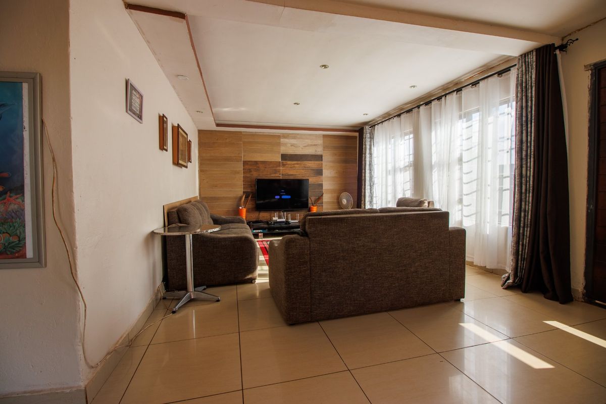 A comfortable living room featuring tiled flooring, recessed ceiling lights, and a wood-paneled feature wall, offering a warm and inviting atmosphere.