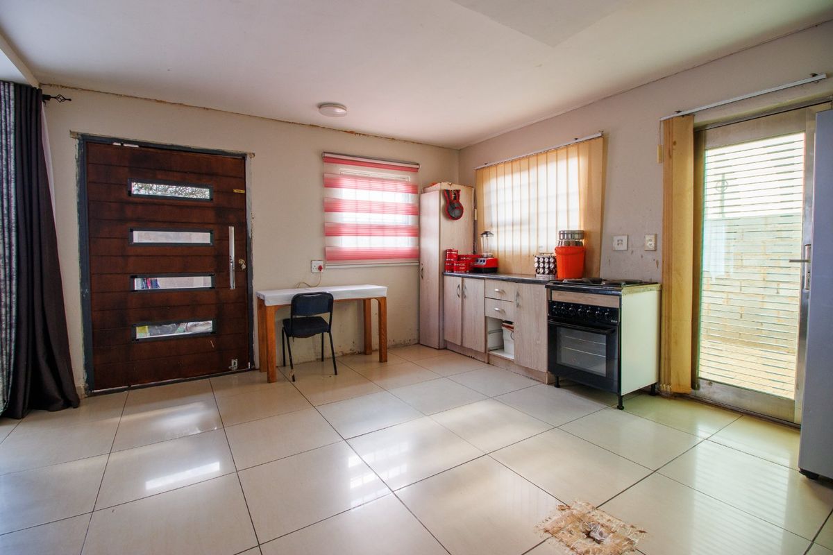 A functional kitchen area featuring tiled flooring, built-in cabinetry, and a freestanding stove, with direct access to both the front entrance and rear exterior.