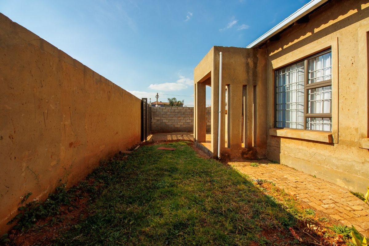 Rear exterior view of the property featuring a small lawn, paved walkway, and a covered porch area with boundary walls.