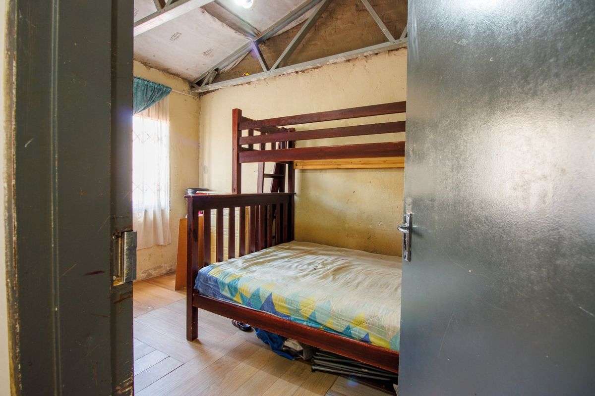 A bedroom featuring exposed roof trusses and laminate flooring, requiring significant cosmetic renovation and wall repairs.