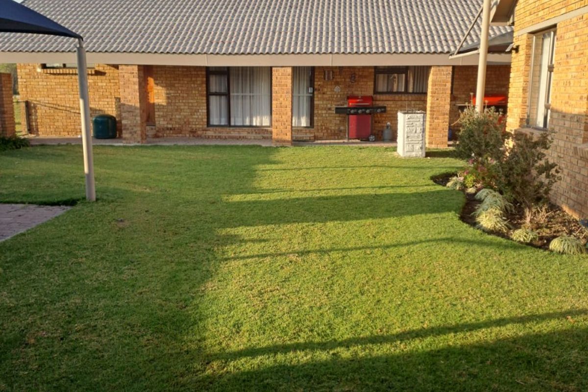 A well-maintained rear exterior view of a brick house featuring a covered patio area and a neat, landscaped lawn.