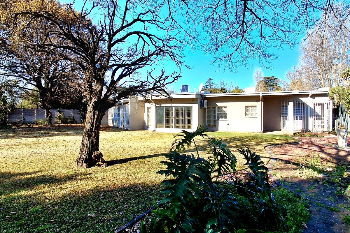 Rear view of the house featuring a spacious garden, paved patio area, security gates, and roof-mounted solar panel.