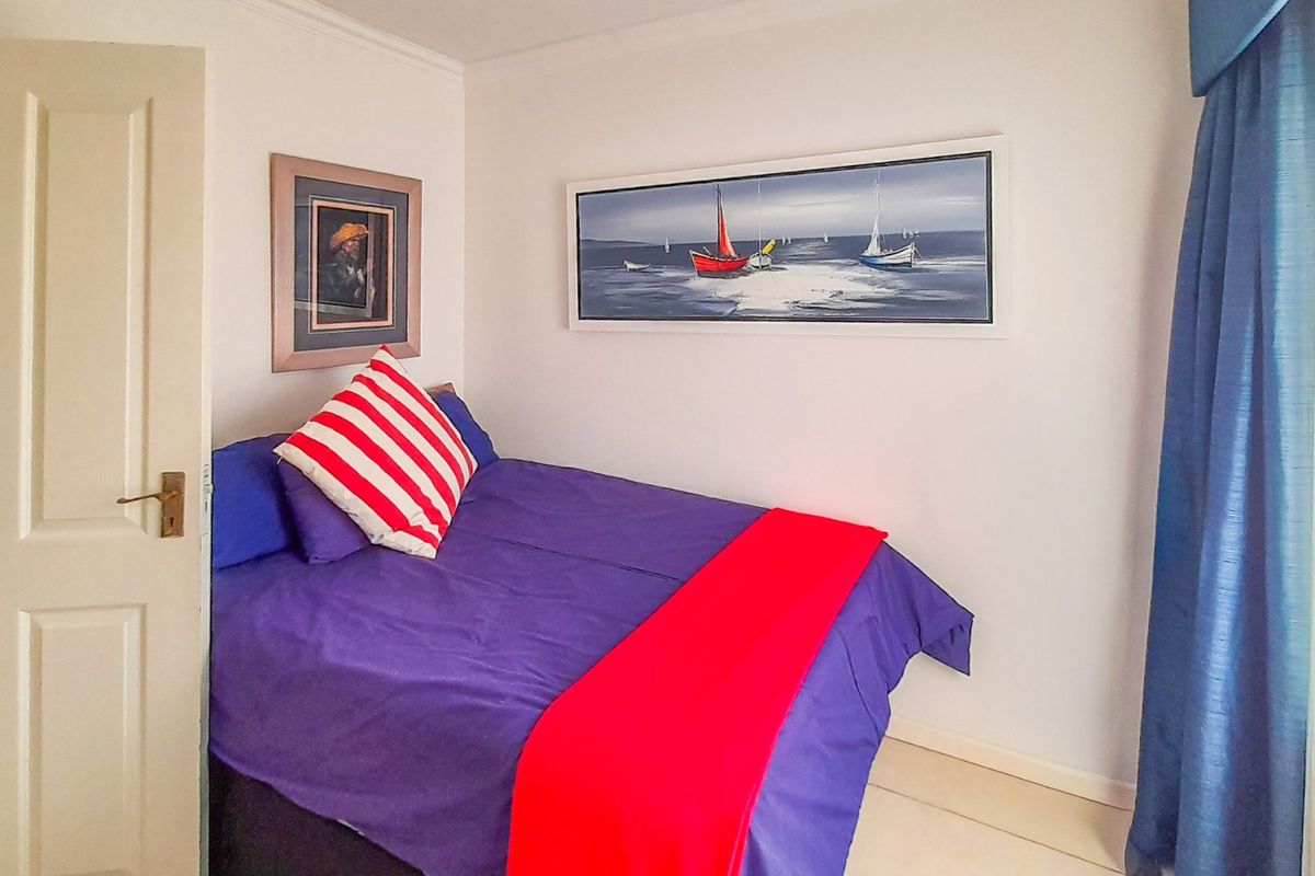 A compact bedroom featuring neutral walls, tiled flooring, and a window dressed with blue curtains.
