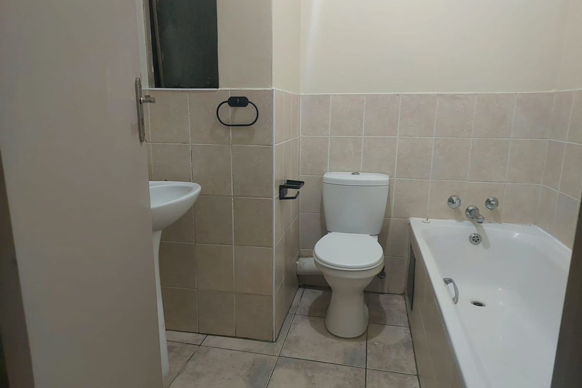 A functional bathroom featuring a pedestal basin, standard toilet, and a bathtub with tiled walls and flooring.