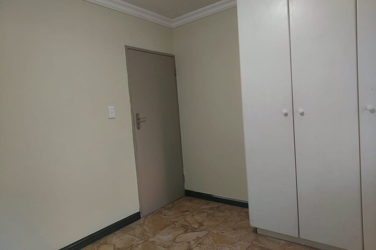 A simple, empty bedroom featuring tiled flooring, a built-in wardrobe, and neutral wall finishes, providing a blank canvas for personalization.