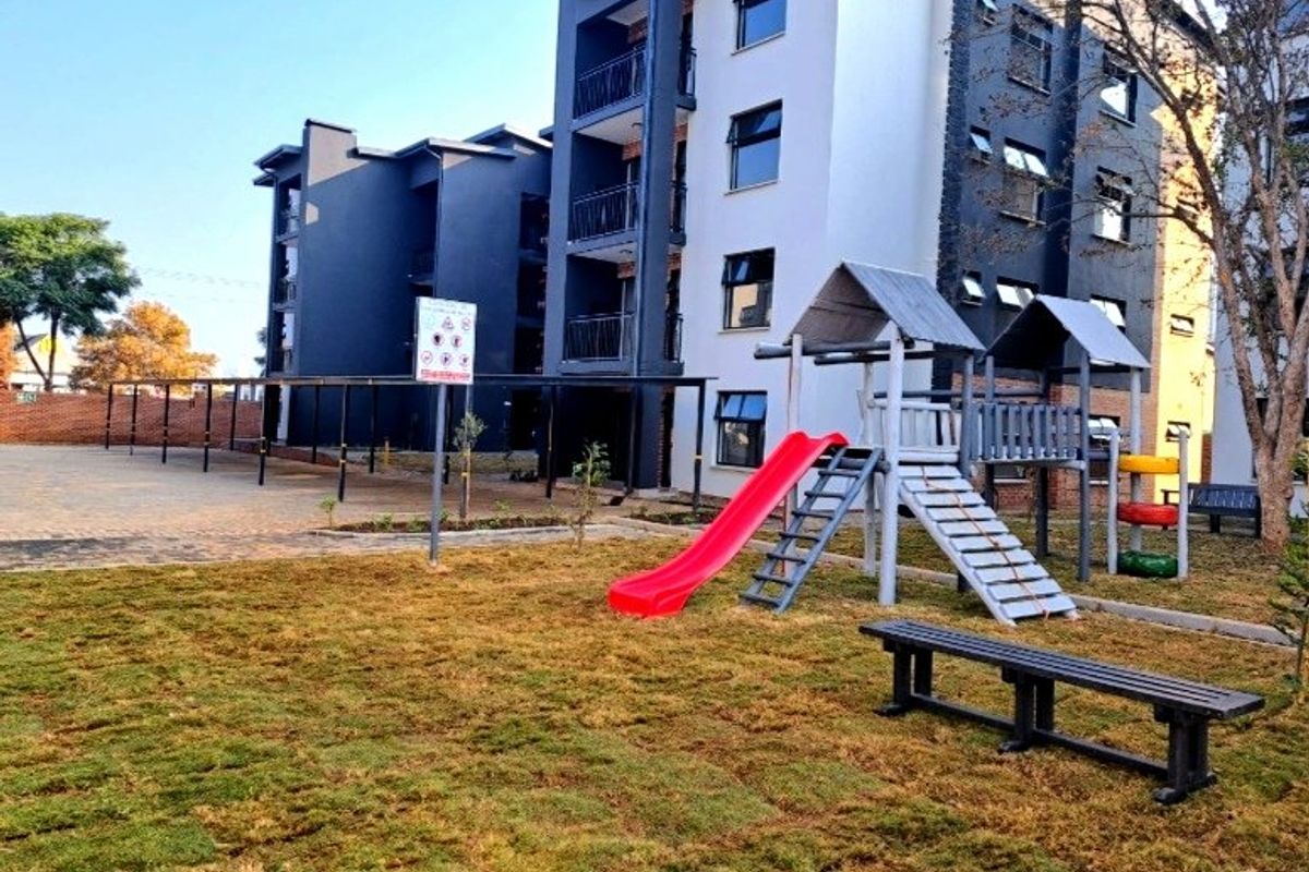 Exterior view of the apartment complex featuring a communal playground area, paved parking carports, and modern multi-story building architecture.