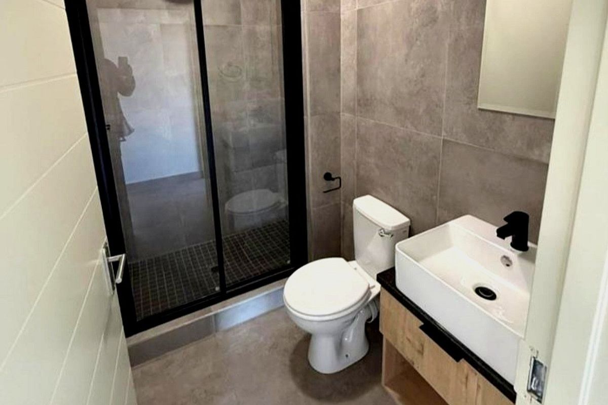 Modern bathroom featuring a walk-in shower with black frame, vessel sink vanity, and neutral floor-to-ceiling tiling.