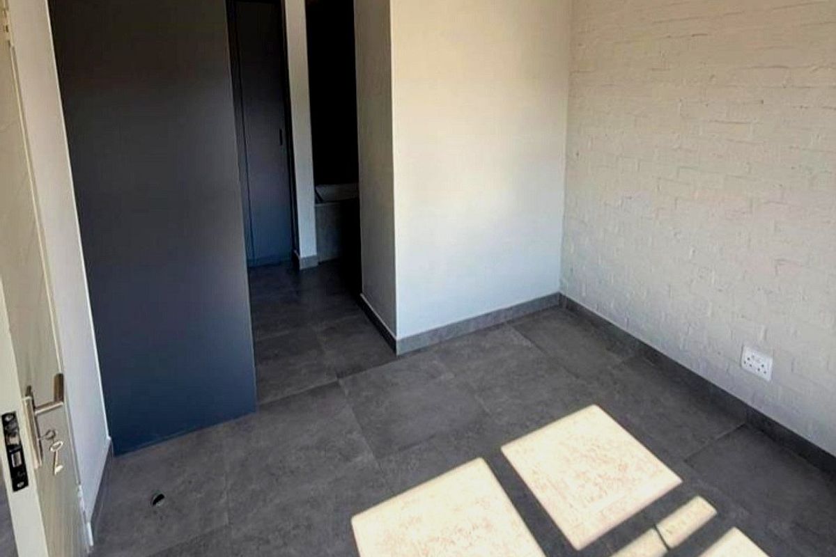 An empty bedroom featuring dark tiled flooring, a painted brick feature wall, and built-in cupboards with a modern dark finish.