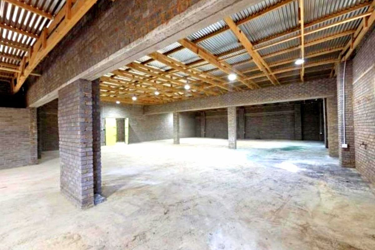 A large, open-plan commercial utility space featuring exposed brick walls, timber roof trusses, and concrete flooring, suitable for industrial or warehouse use.