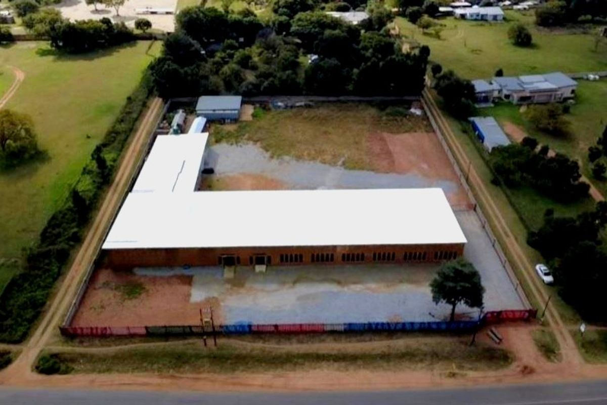 Aerial view of a commercial property featuring a large warehouse-style building with a metal roof, set within a fenced perimeter with ample yard space.