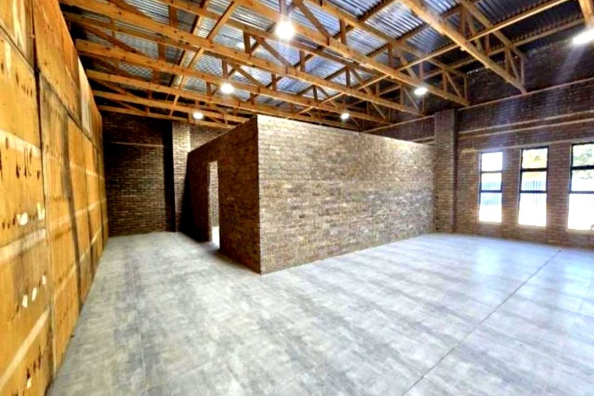Spacious open-plan commercial area featuring exposed timber roof trusses, industrial-style brick walls, tiled flooring, and abundant natural light from large windows.
