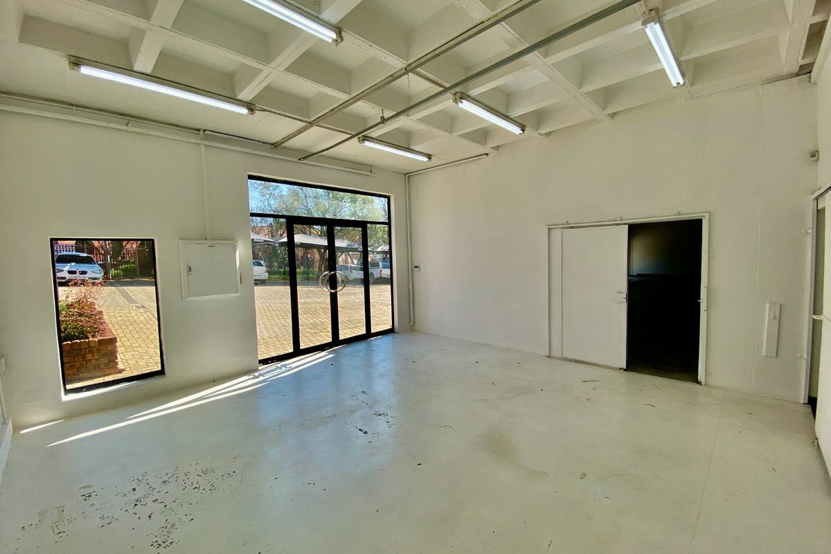 Spacious industrial utility area featuring an exposed waffle slab ceiling, fluorescent lighting, painted concrete flooring, and large glass entrance doors providing natural light.