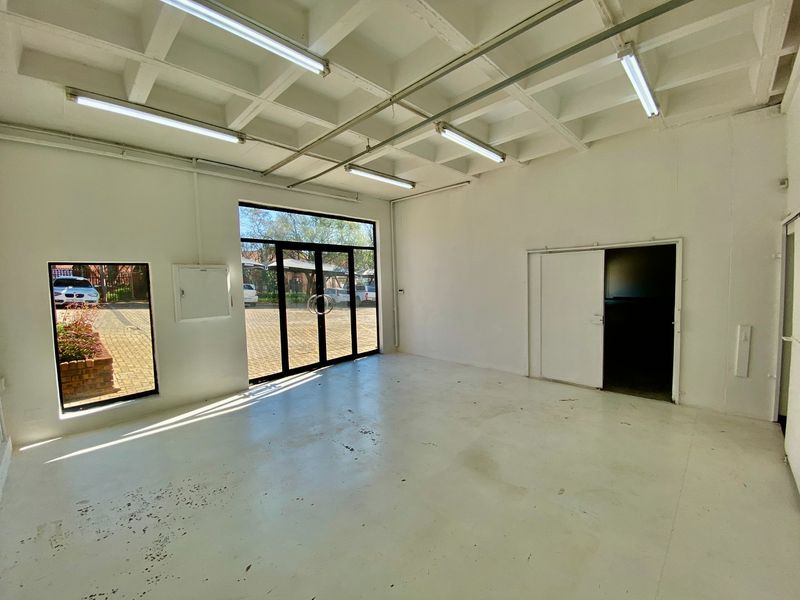 Spacious industrial utility area featuring an exposed waffle slab ceiling, fluorescent lighting, painted concrete flooring, and large glass entrance doors providing natural light.
