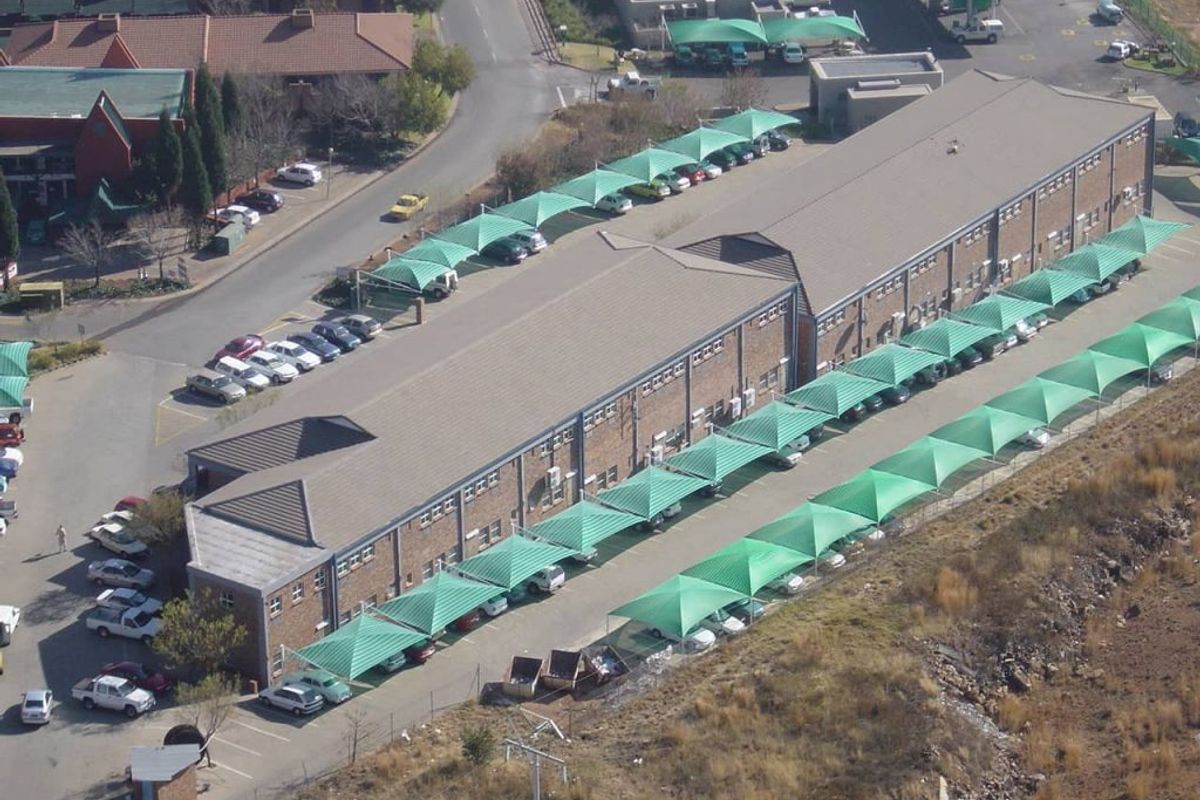 Aerial view of an industrial property featuring a long brick building with extensive shade cloth covered parking bays and paved access areas.