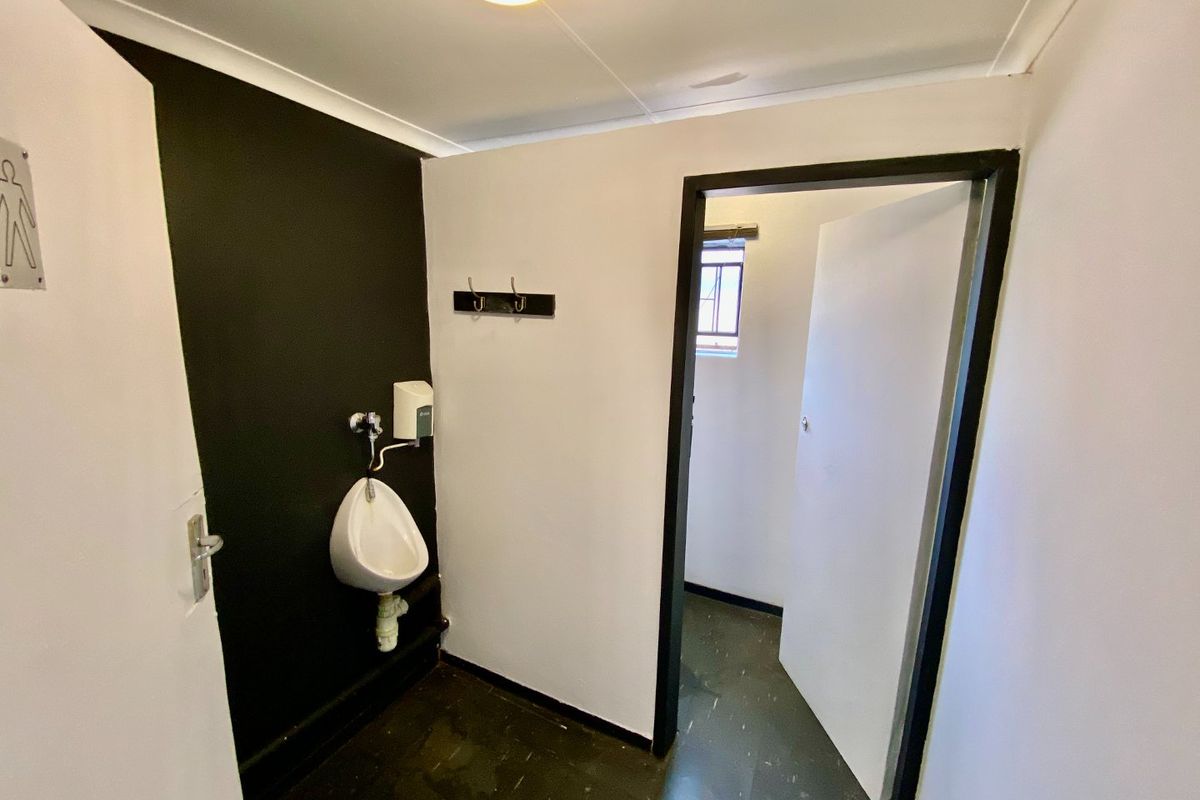 A functional industrial-style restroom featuring a wall-mounted urinal, soap dispenser, and durable vinyl flooring.