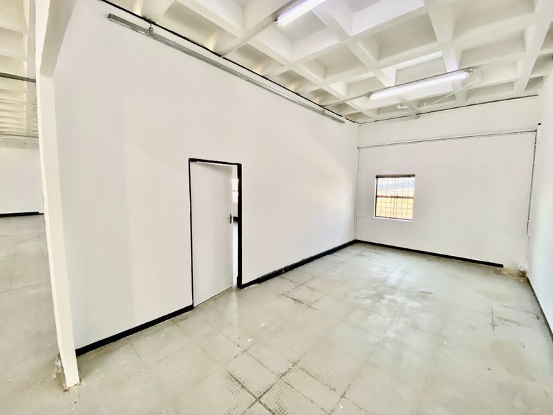 An empty industrial utility space featuring a waffle slab ceiling, fluorescent lighting, and a security-barred window, suitable for storage or workshop use.