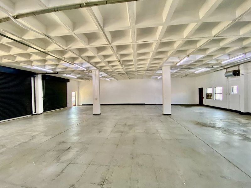 Spacious industrial warehouse unit featuring a high waffle slab ceiling, concrete flooring, and large roller shutter doors for easy access.
