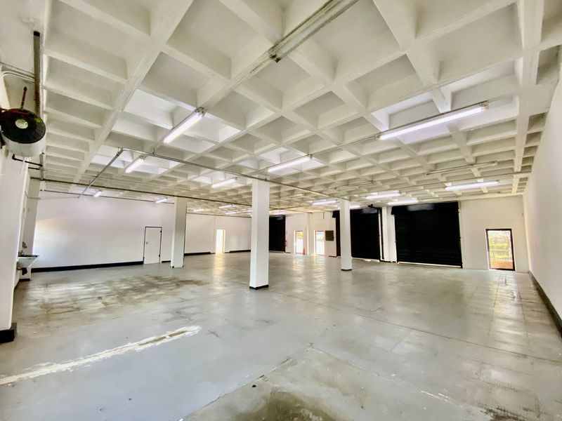 Spacious industrial warehouse area featuring a waffle slab ceiling, concrete flooring, structural columns, and multiple roller shutter doors for easy access.