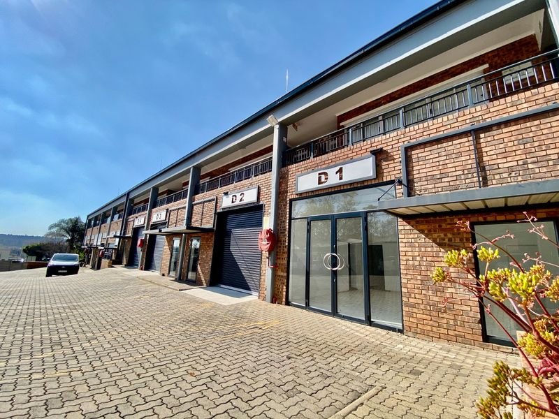 Exterior view of a modern industrial complex featuring face brick facade, roller shutter doors, glass storefront entrances, and a paved parking area.
