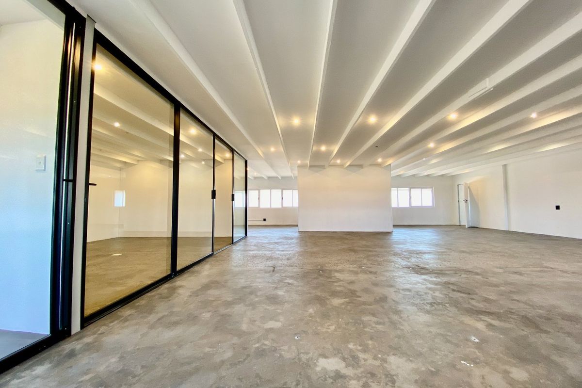 Spacious open-plan commercial office area featuring polished concrete floors, exposed beam ceilings, and modern black-framed glass partitioning for private meeting spaces.