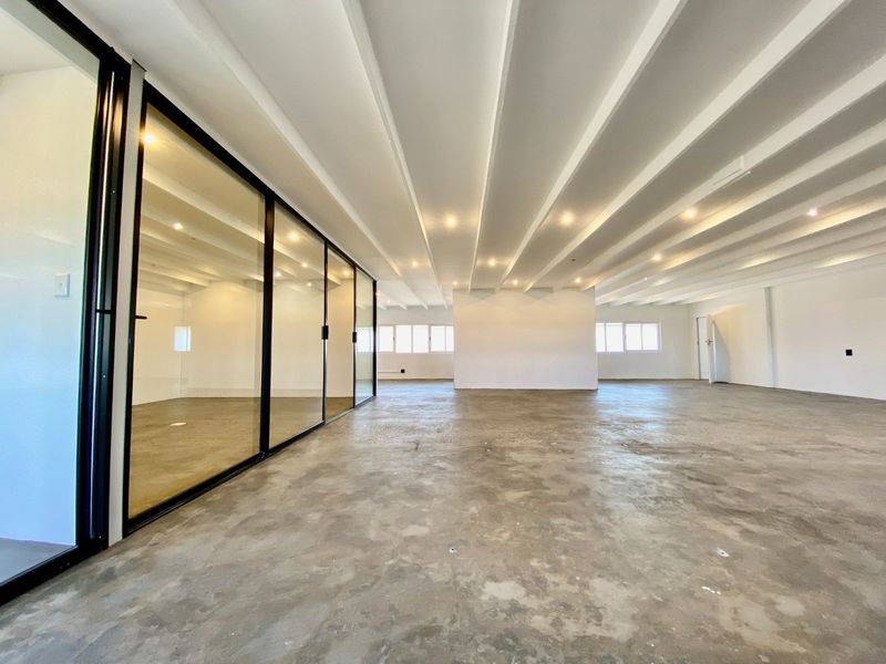 Spacious open-plan commercial office area featuring polished concrete floors, exposed beam ceilings, and modern black-framed glass partitioning for private meeting spaces.