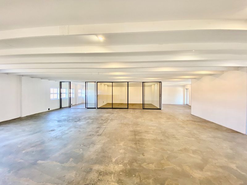 Spacious open-plan commercial area featuring exposed ceiling beams, polished concrete flooring, and modern black-framed glass partitions for flexible office or retail use.