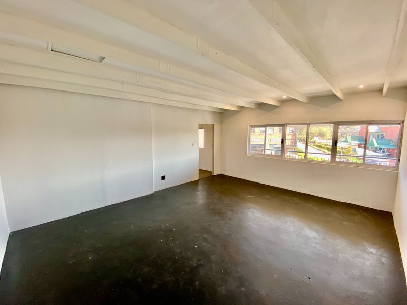 An empty, open-plan office space featuring exposed beam ceilings, large windows providing natural light, and a raw concrete floor finish.