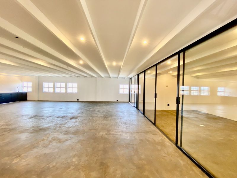 Spacious open-plan commercial area featuring polished concrete floors, exposed beam ceilings, and modern black-framed glass partitioning for versatile office or studio use.