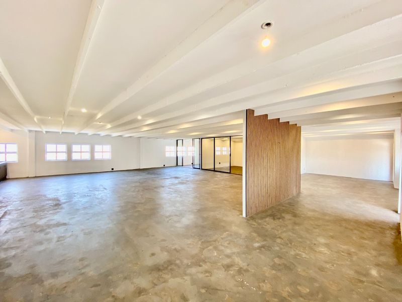 Spacious open-plan commercial office area featuring polished concrete floors, exposed beam ceilings, and a modern slatted timber feature wall with glass partitions.
