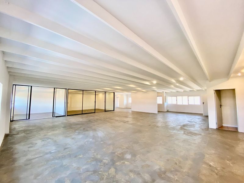 Spacious open-plan commercial office area featuring exposed beam ceilings, polished concrete flooring, and modern glass partition walls for flexible workspace configuration.