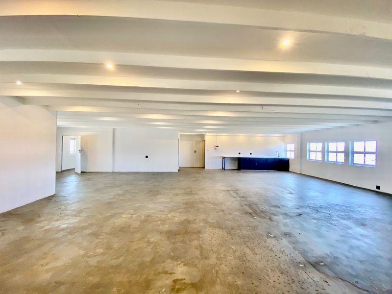Spacious open-plan commercial area featuring exposed beam ceilings, recessed lighting, and a functional kitchenette corner with concrete flooring throughout.