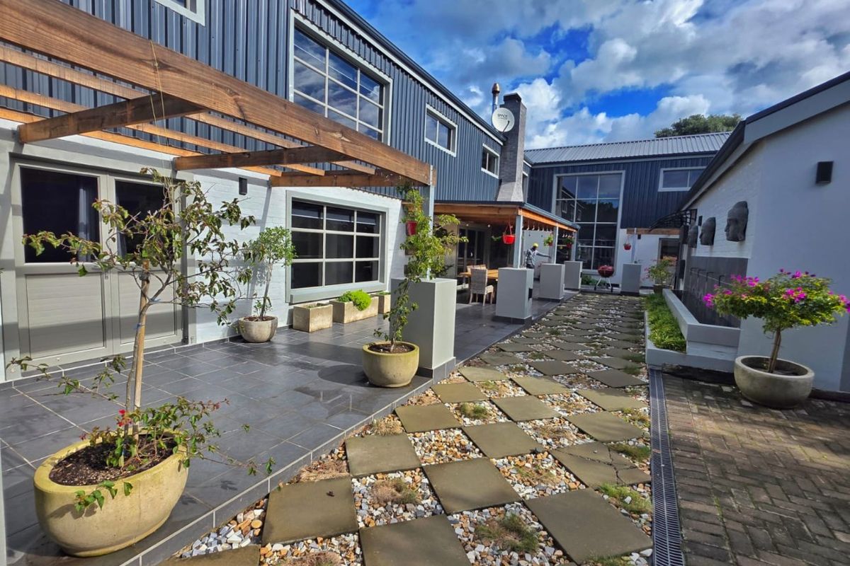 A modern rear courtyard featuring a tiled patio with a timber pergola, stone paver walkway, and contemporary metal-clad building exterior.