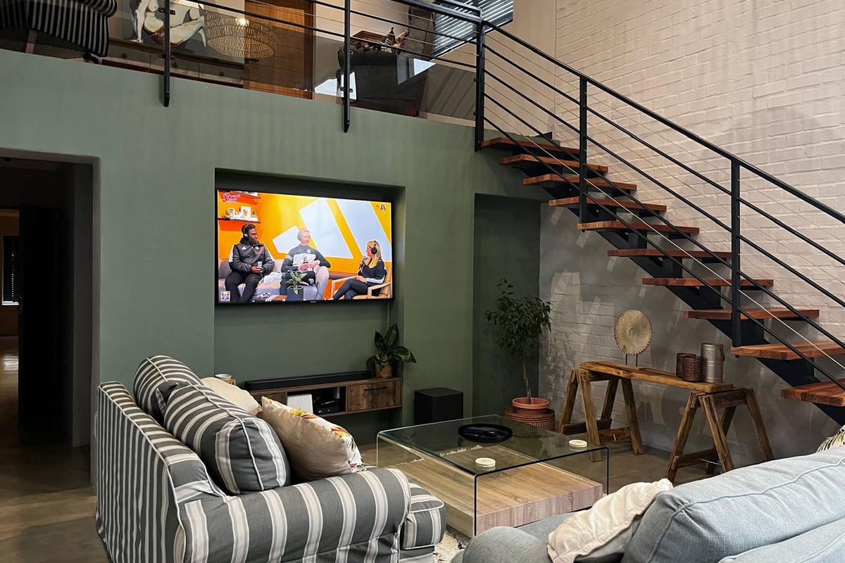 Modern living room featuring a striking open-tread staircase with metal balustrades, a recessed television niche, and a mezzanine level overlooking the space.