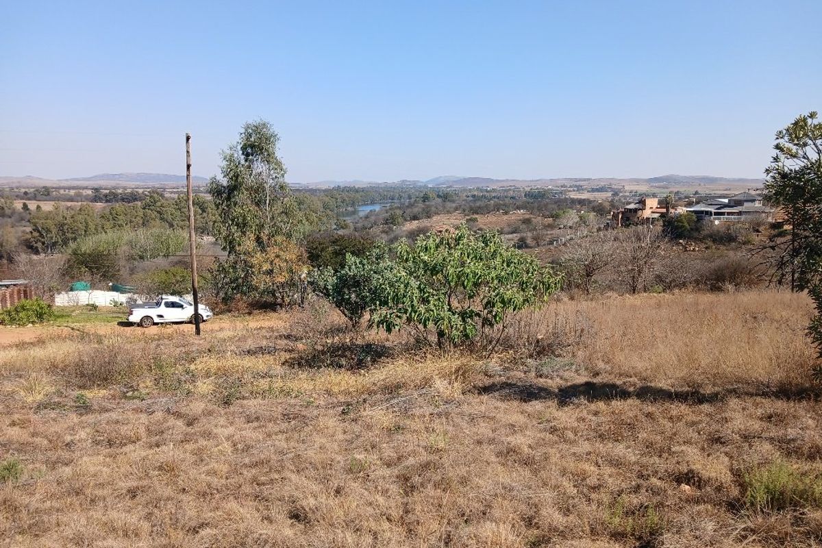 A wide-angle view of the vacant residential land, showcasing the surrounding landscape, natural vegetation, and distant river scenery.