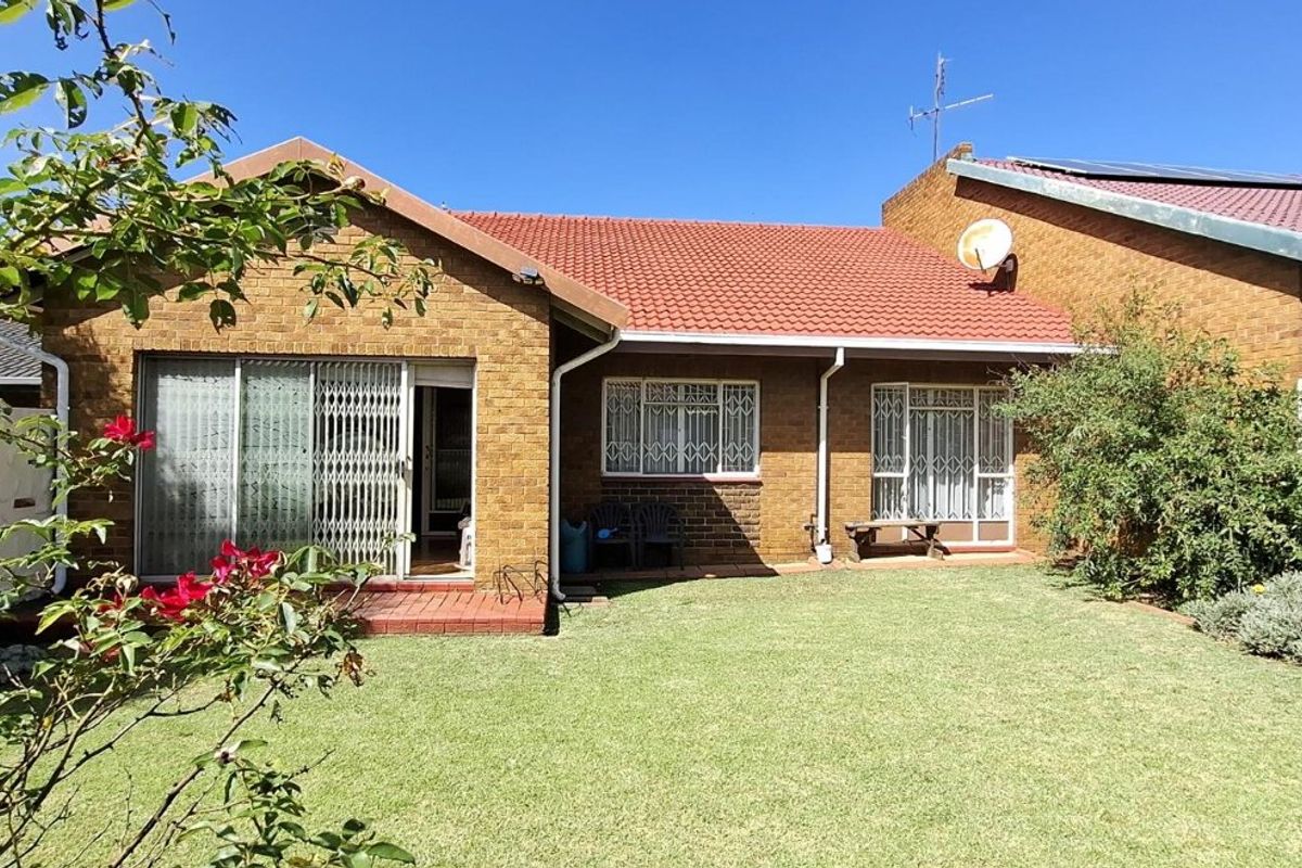 Rear view of a face brick house featuring a tiled roof, sliding doors with security gates, and a well-maintained garden.