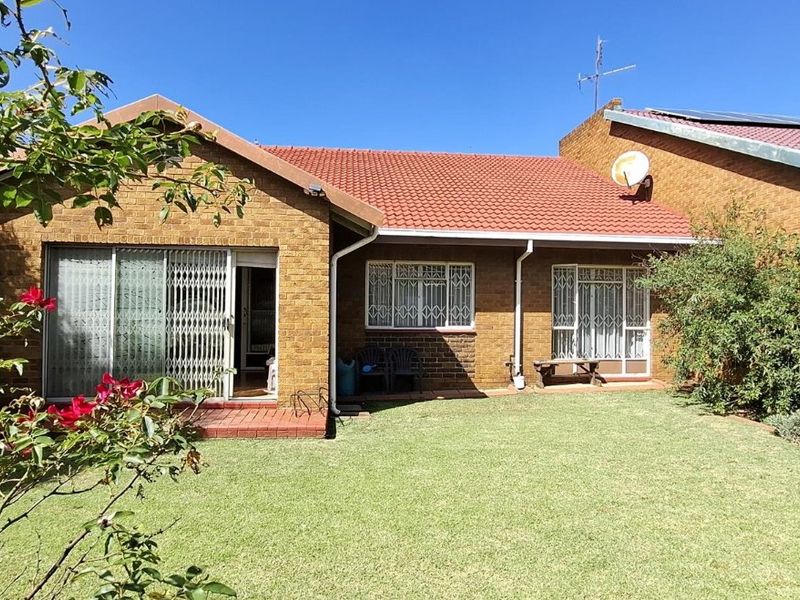 Rear view of a face brick house featuring a tiled roof, sliding doors with security gates, and a well-maintained garden.