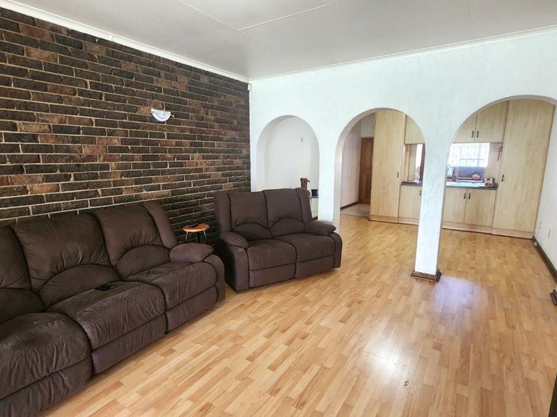 Open plan living area featuring an exposed brick wall, arched architectural details, and laminate flooring, flowing into a kitchen space with built-in cabinetry.