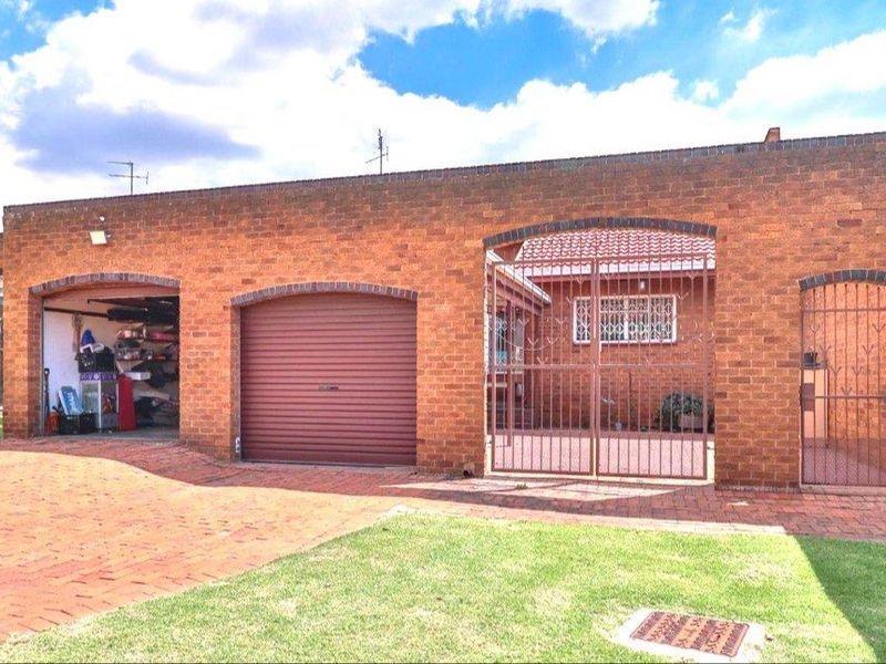 Front exterior view of a brick house featuring multiple roller garage doors, a paved driveway, and a secure gated entrance.