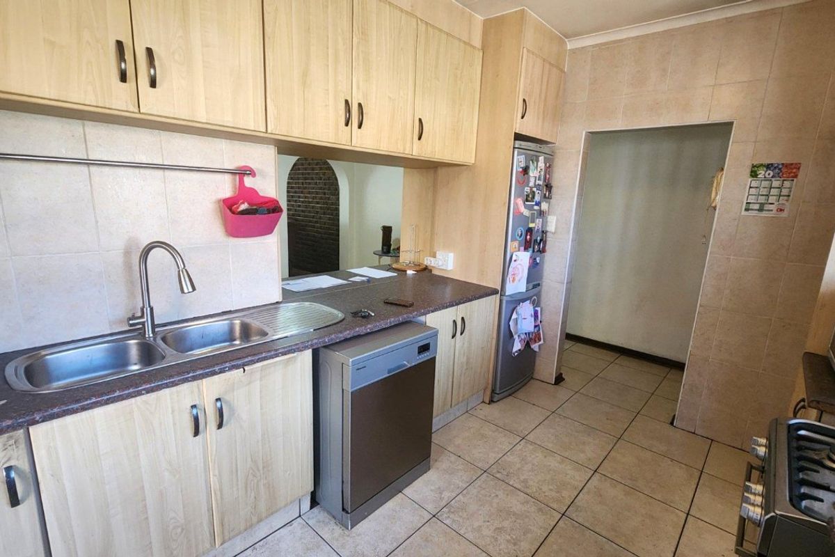 A functional kitchen featuring light wood-look cabinetry, tiled splashbacks, tiled flooring, and a double bowl stainless steel sink with integrated appliances.