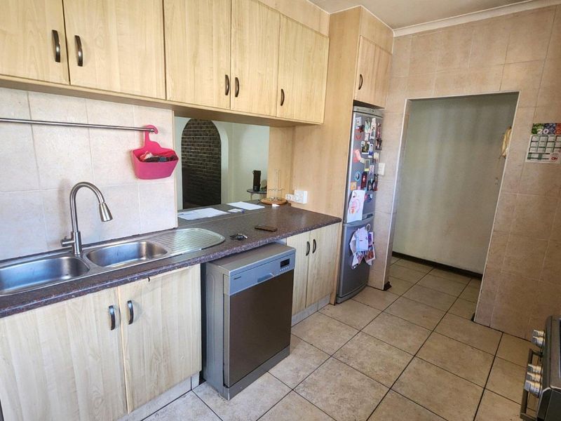 A functional kitchen featuring light wood-look cabinetry, tiled splashbacks, tiled flooring, and a double bowl stainless steel sink with integrated appliances.