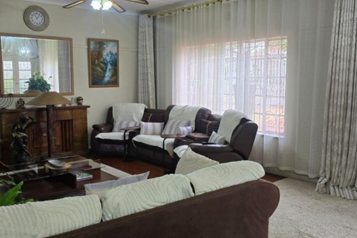 A comfortable living room featuring hardwood flooring, a ceiling fan, and large windows with security gates, offering a bright and functional living space.