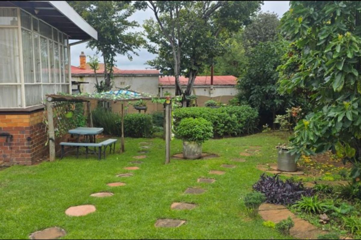 A rear garden view featuring a brick-based sunroom, a stone-stepped pathway, and established greenery within a private boundary wall setting.