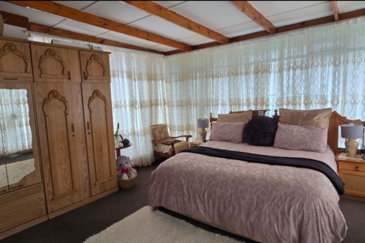 A bedroom featuring exposed timber ceiling beams, carpeted flooring, and a large fitted wardrobe, offering a traditional aesthetic with ample natural light.
