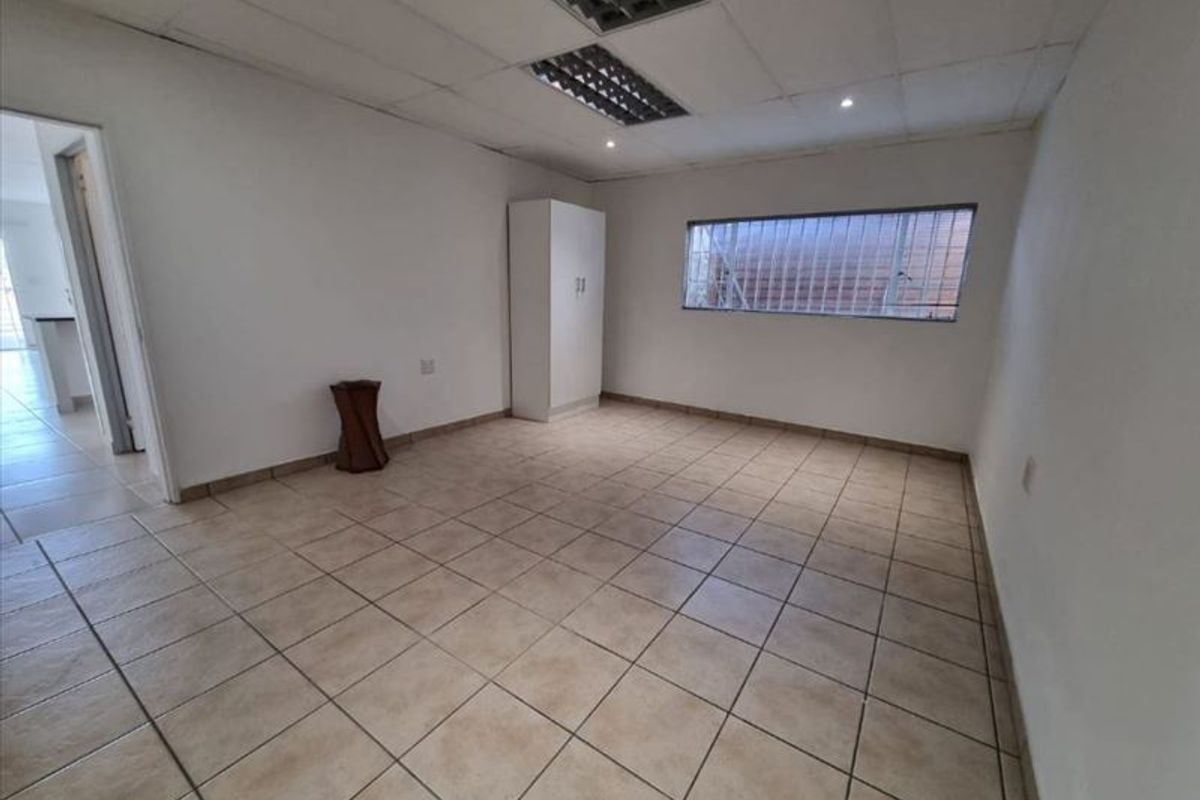 A spacious, empty bedroom featuring tiled flooring, a drop ceiling with recessed lighting, and a window fitted with security bars.