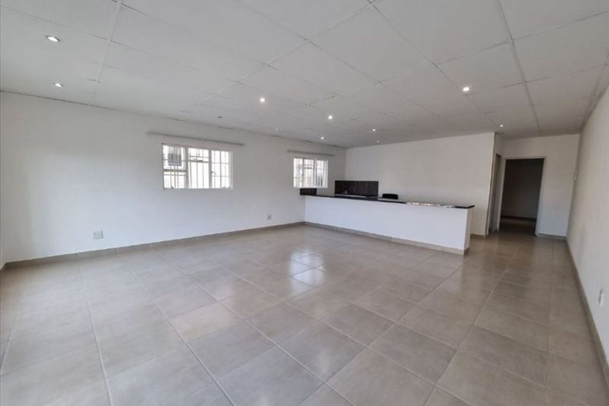 Spacious open-plan living area featuring tiled flooring, a drop ceiling with recessed lighting, and a built-in breakfast bar.