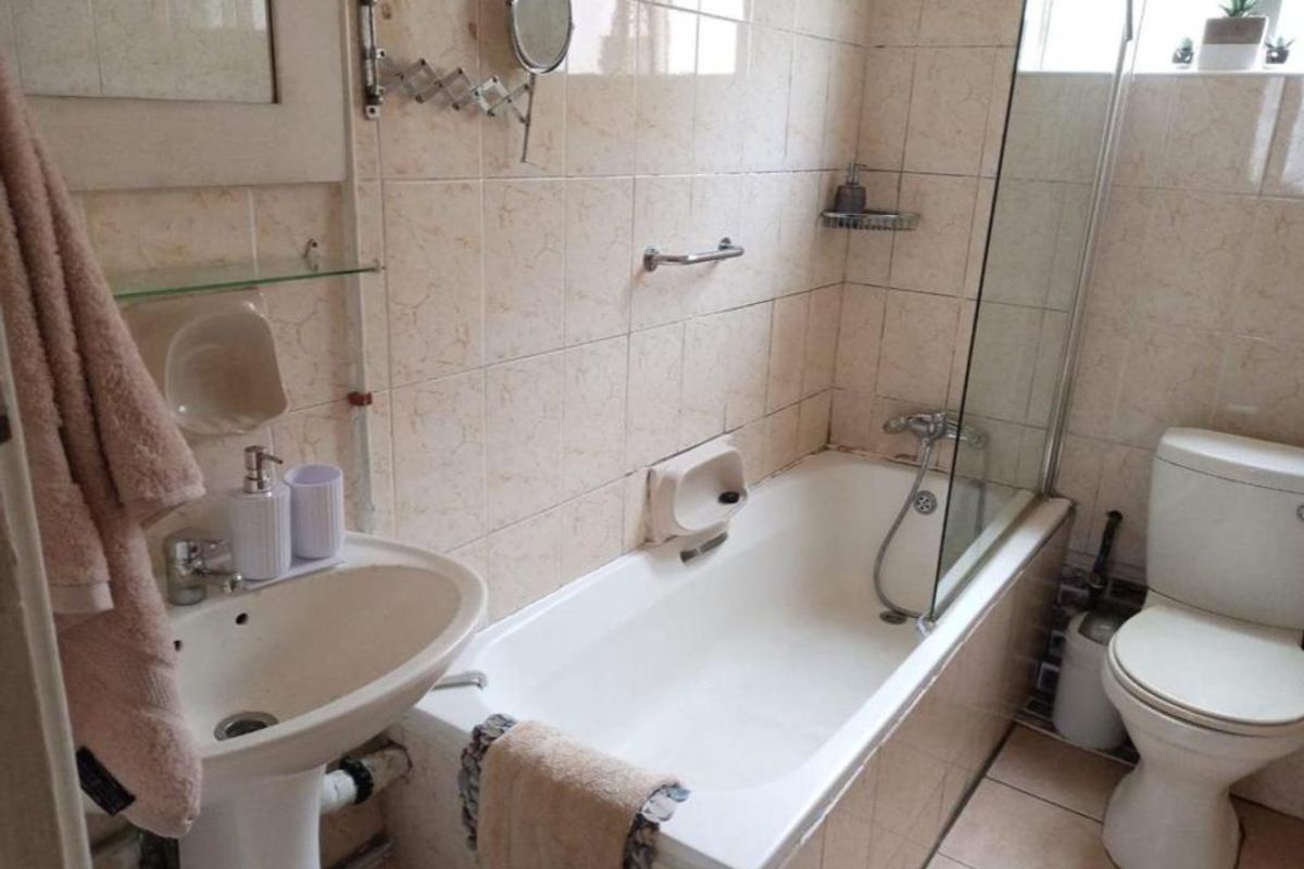 A functional bathroom featuring a pedestal basin, bathtub with glass screen, and toilet, finished with neutral wall and floor tiling.