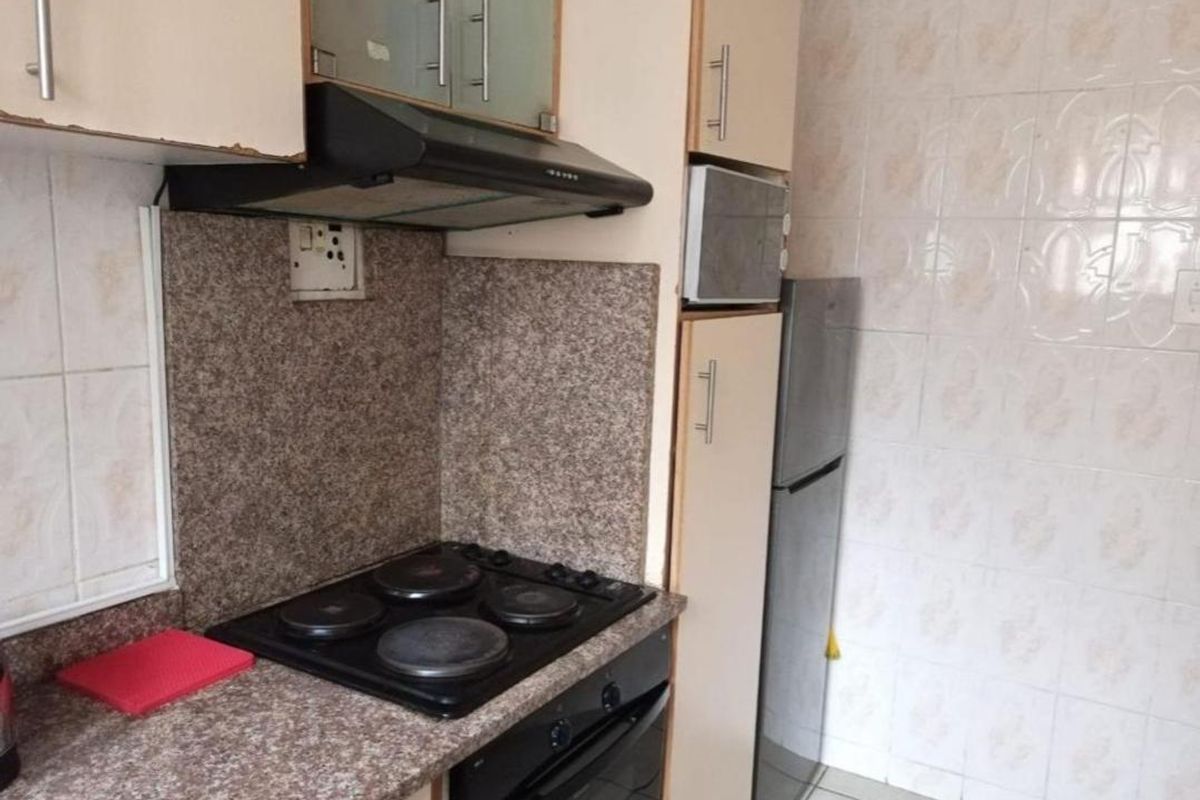 Compact kitchen featuring built-in cabinetry, laminate countertops, an electric hob, oven, and extractor fan with tiled wall finishes.