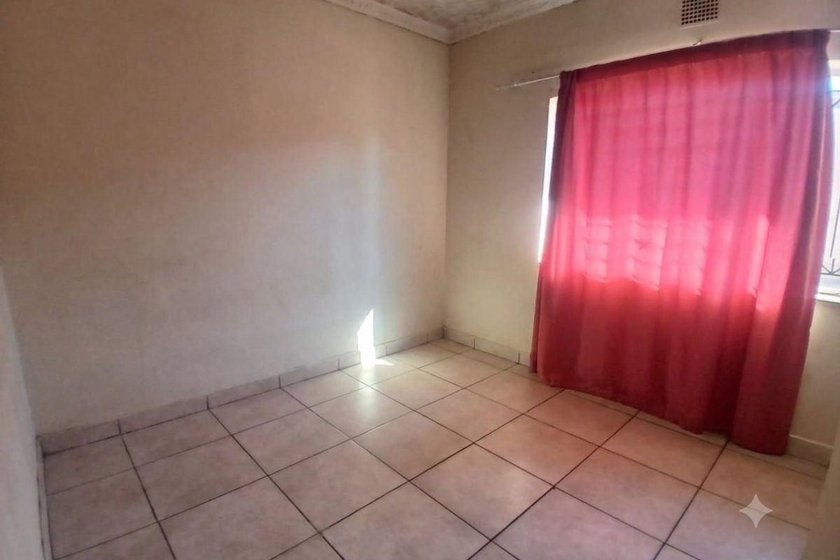 An empty bedroom featuring tiled flooring, ceiling cornice detailing, and security bars on the window.